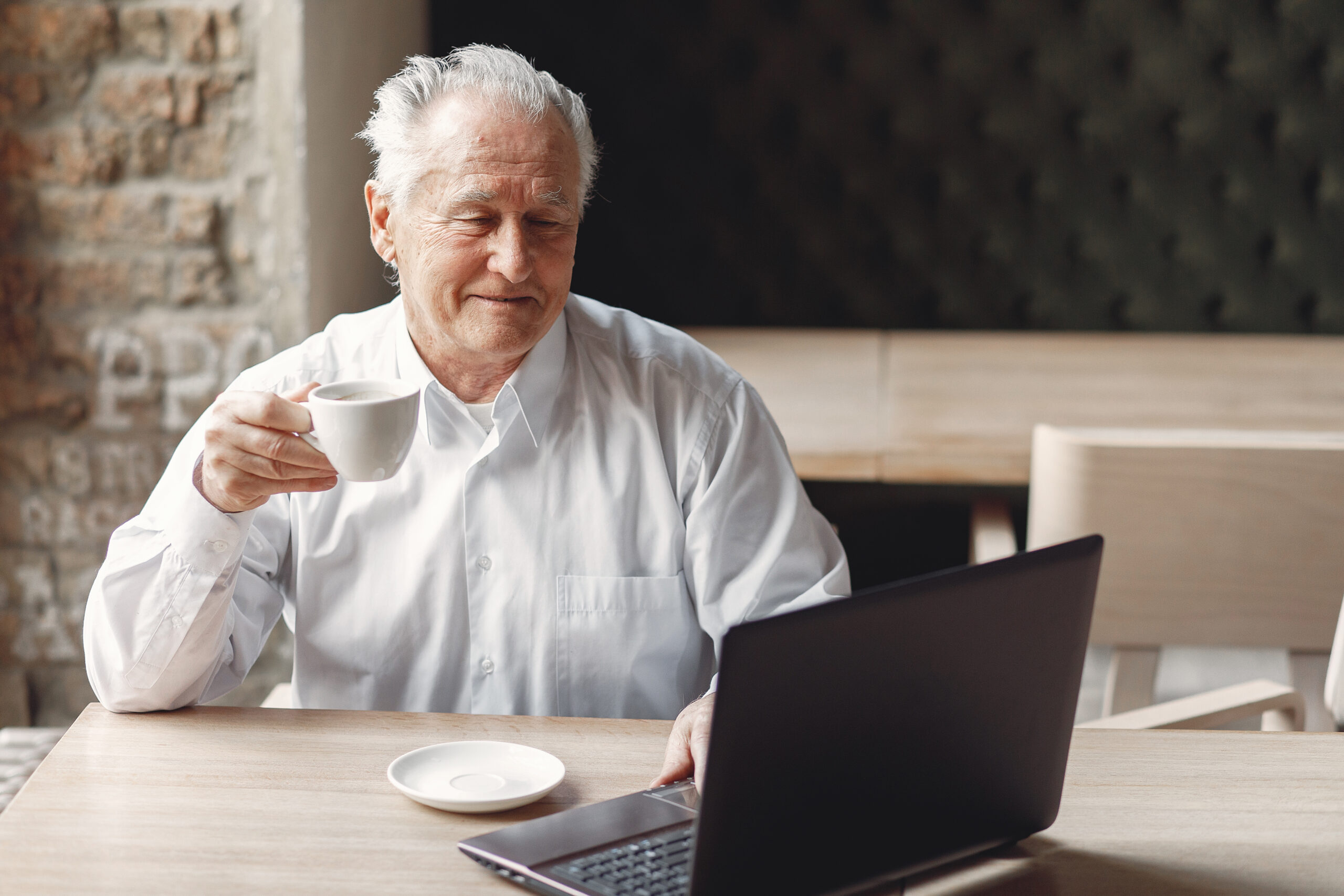 Мужчина пенсионер сидит за компьютером и пьет чашку кофе во время занятия хобби