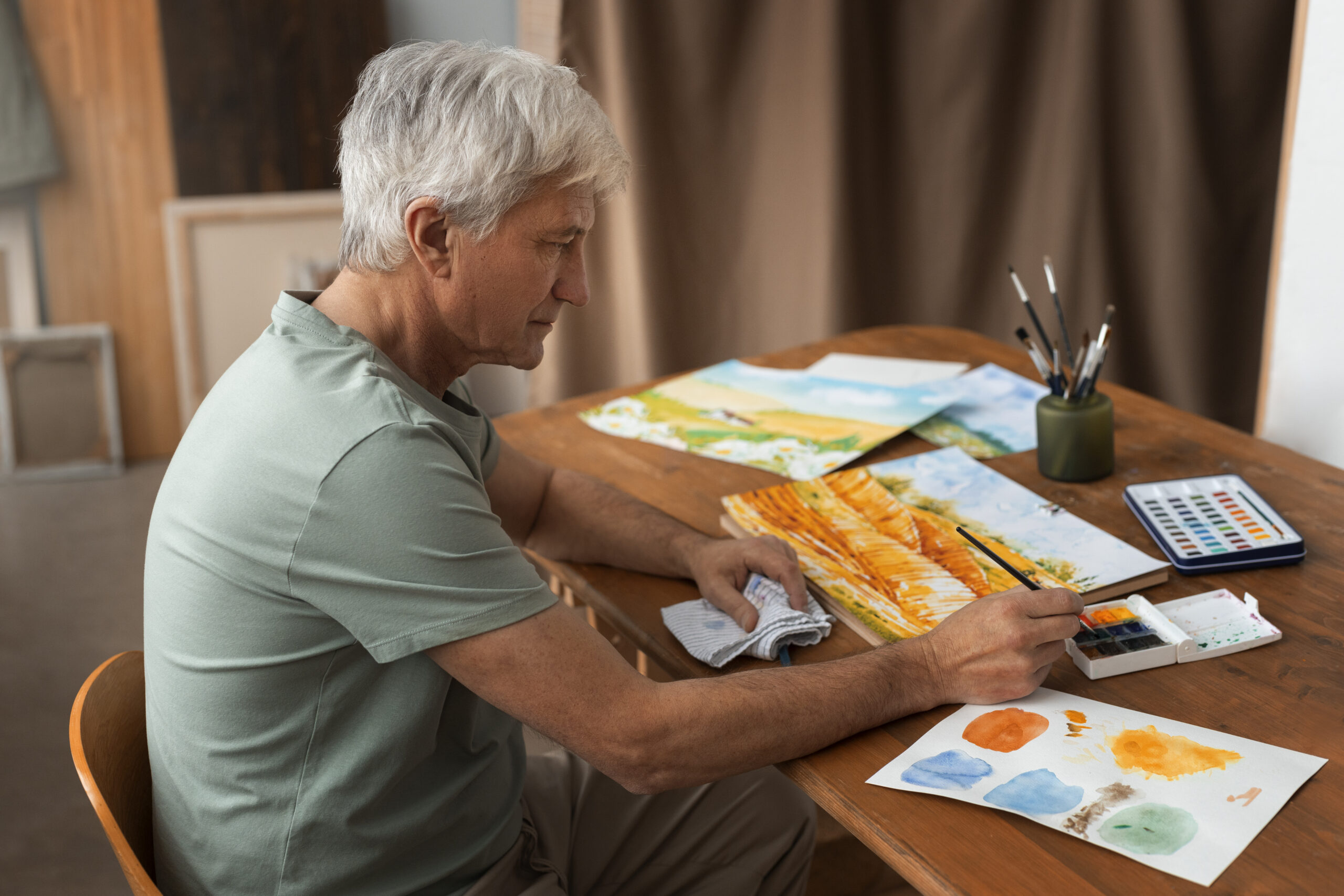 мужчина пенсионер сидит за столом и занимается своим новым хобби рисованием